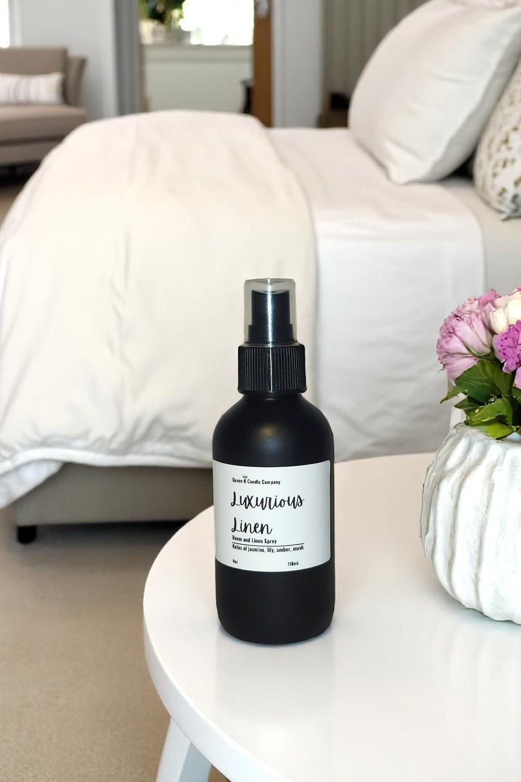 Black spray bottle labeled 'Luminous Linen' on a white table with a blurred living room background.