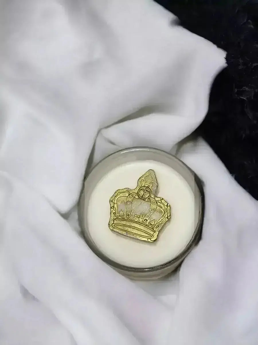 Queen Wickless Candle Jar with a golden crown design on top, resting on a soft white fabric.