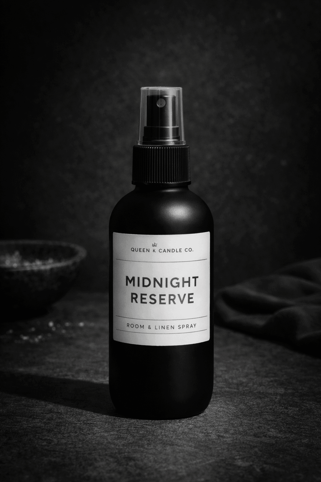 Black room and linen spray bottle labeled 'Midnight Reserve' by Queen & Candle Co. on a dark background.