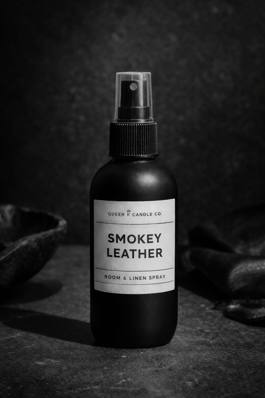 Black room spray bottle labeled 'Smokey Leather' on a dark background