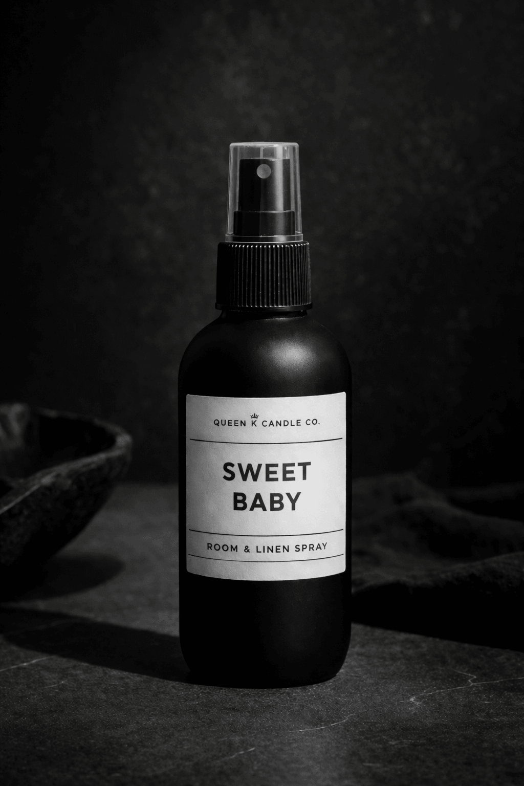 Black room spray bottle labeled 'Sweet Baby' on a dark background
