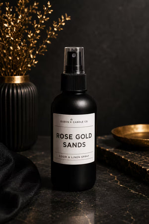 Black spray bottle labeled 'Rose Gold Sands' on a dark surface with decorative elements.