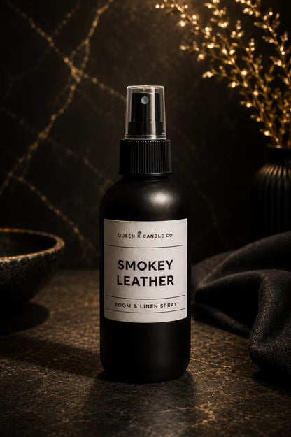 Black room & linen spray bottle labeled 'Smokey Leather' by Queen & Candle Co. on a dark surface with decorative elements.